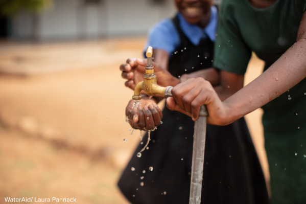 Two girls washing hands under running water pipe